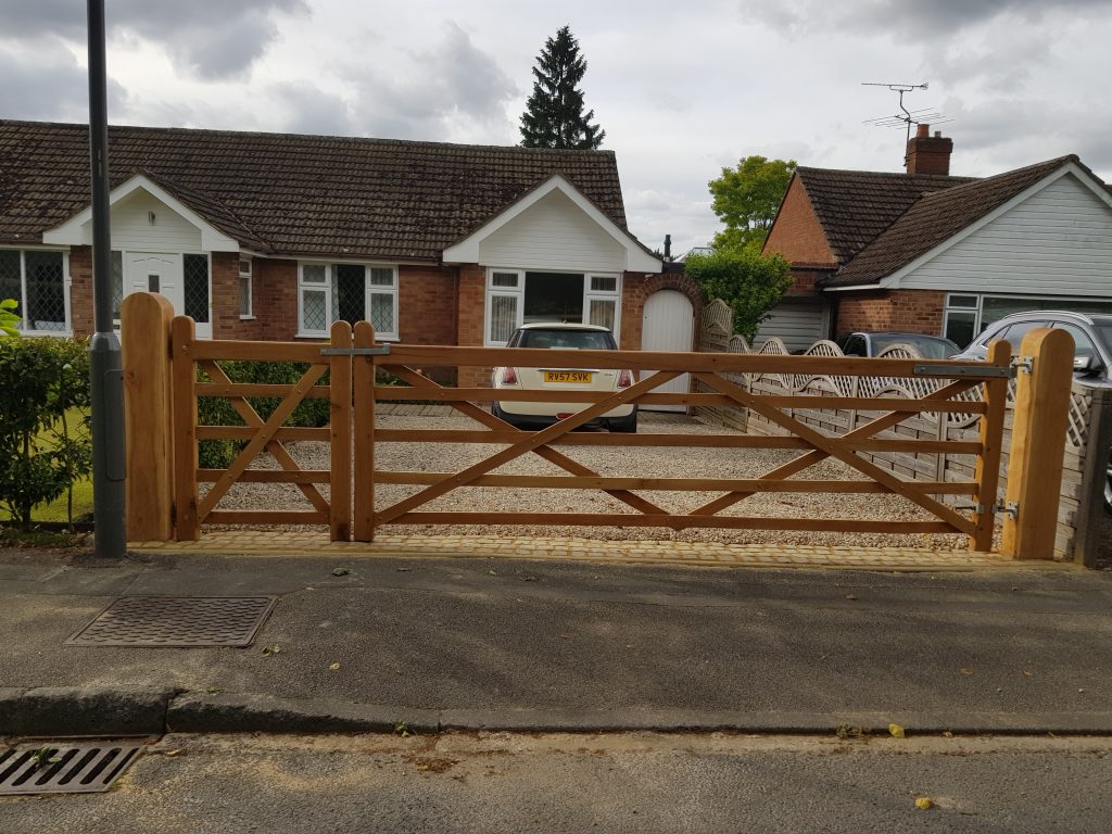 A house with a beige gravel driveway which has oak field gates with 5 bars and a smaller gate on the side with european oak gate posts to keep them up, creating a beautiful boundary with cohesiveness.