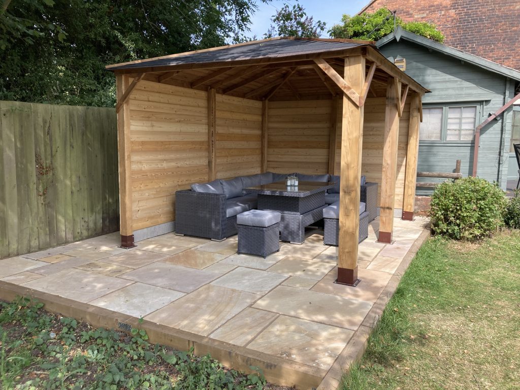 An outdoor seating area created using Siberian Larch Fence Posts and Halflap Cladding with outdoor furniture underneath.