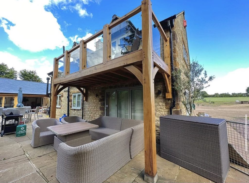 oak beams used to create a glass protected balcony overlooking a back garden